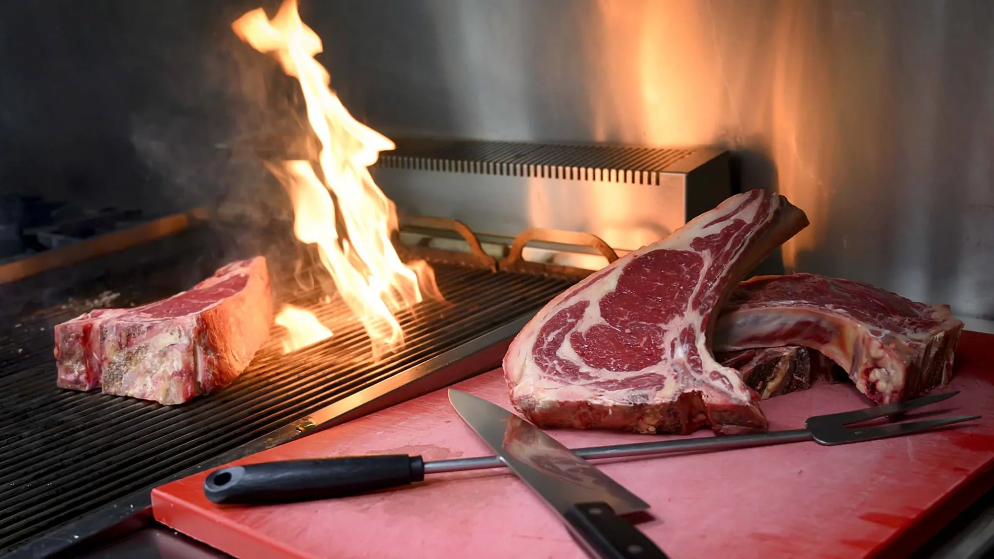 Chuletones de vaca madurada sobre la parrilla de Plaché, con las llamas vivas al fondo